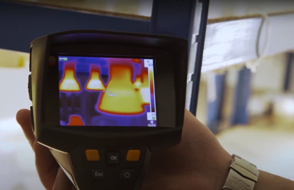 A close-up photograph of a thermal imaging camera displaying colourful thermal patterns on a screen. The camera is pointed towards a surface, revealing temperature variations through different hues. The image suggests the use of thermal imaging technology for heat detection or monitoring purposes.