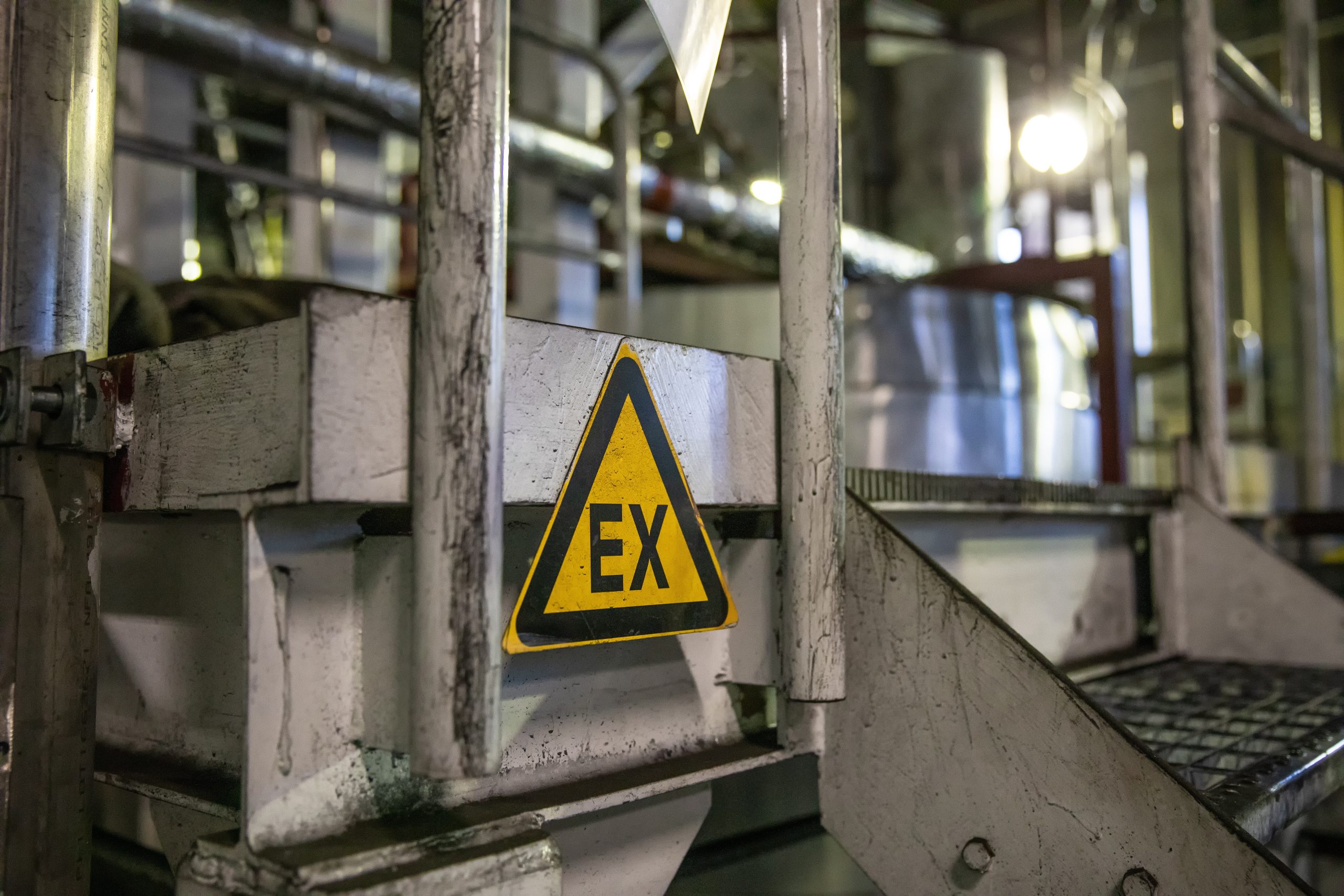 A view of an ATEX hazardous area with industrial equipment and warning signs. The area is designated as hazardous due to the presence of potentially explosive atmospheres. The image conveys the concept of industrial safety and the need for specialized equipment and precautions in hazardous environments.