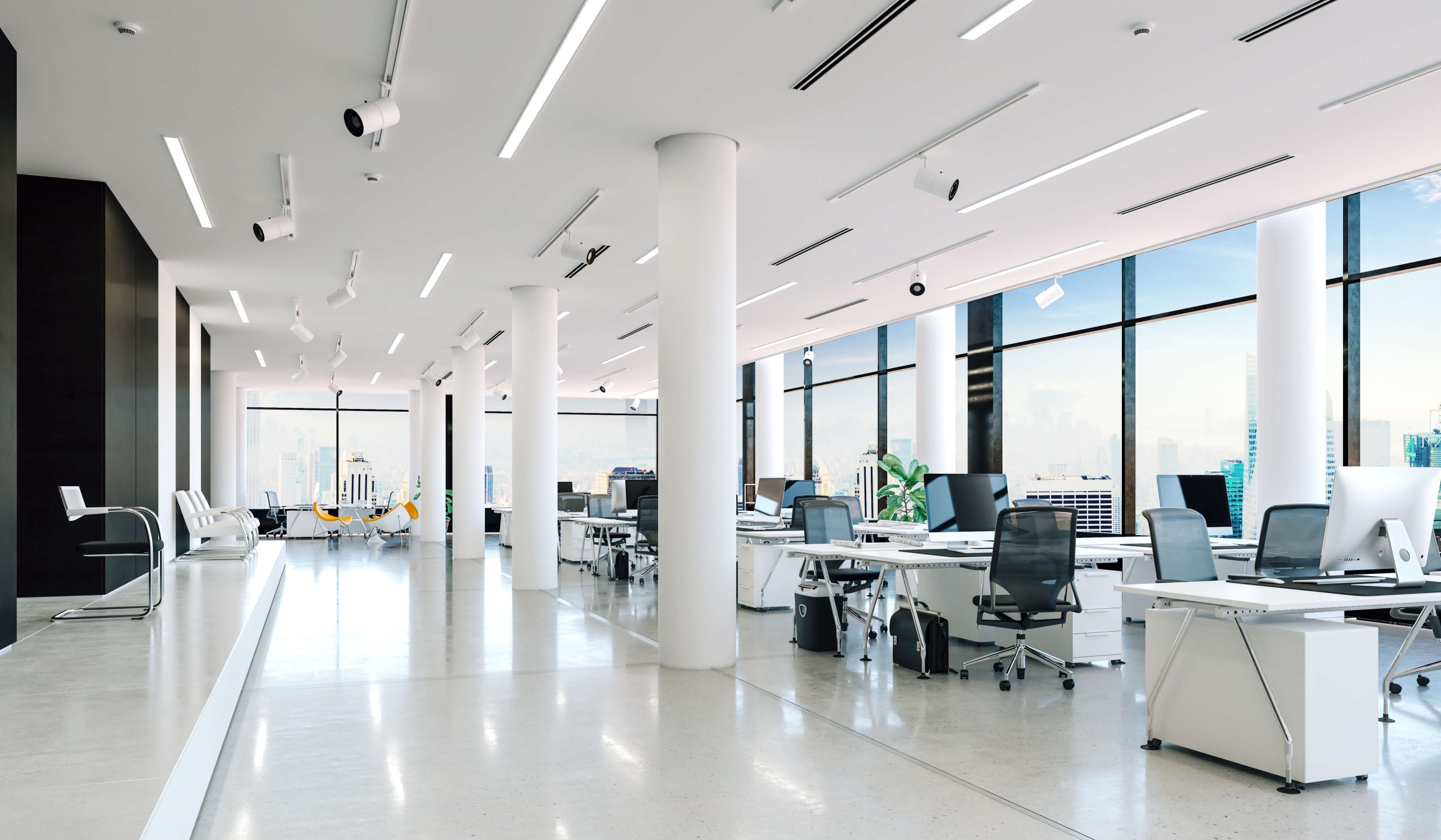 A modern commercial office space with desks, chairs, and computer monitors arranged in an open-plan layout. Large windows provide ample natural light, and plants add a touch of greenery to the space. The image conveys the concept of a contemporary and productive work environment in a commercial setting.