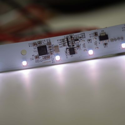 A close-up photograph showing an LED strip. The strip consists of multiple LED lights arranged in a linear configuration. The image conveys the concept of LED strip lighting technology.
