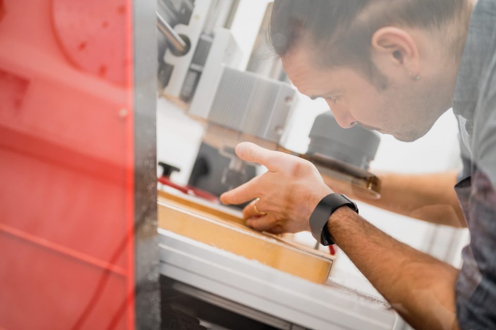 A person working in a modern workshop environment. They are focused on a task, possibly inspecting or assembling components. The workshop features industrial machinery and equipment, suggesting a setting for manufacturing or engineering activities.